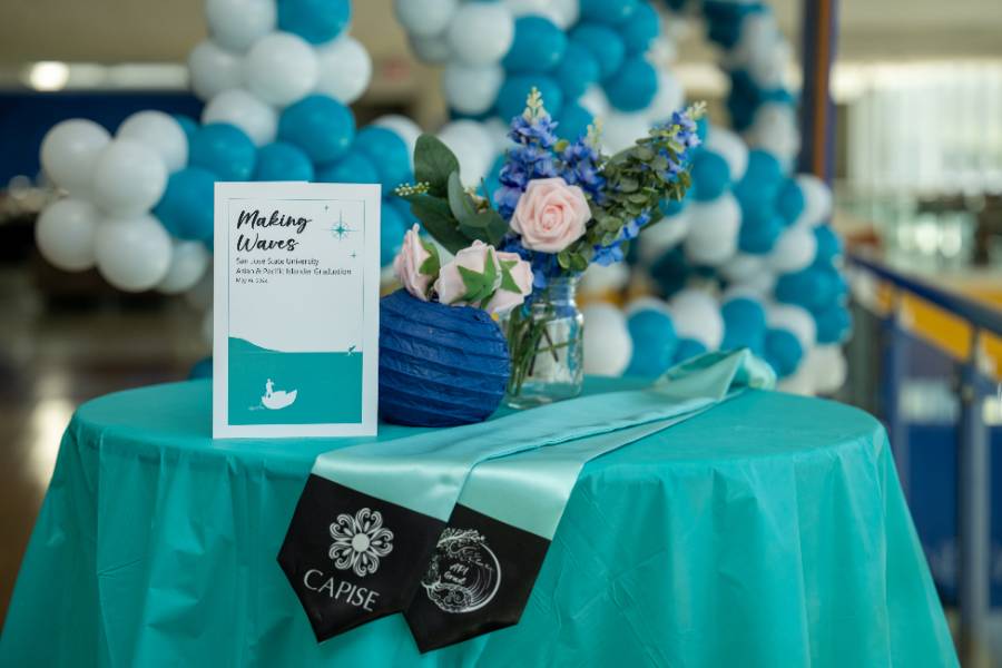 Making Waves: API Graduation Round table with blue tablecloth and flower centerpiece with API Graduation program and API Graduation stole displayed on table.