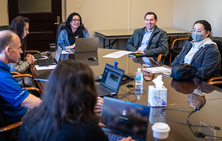 Six individuals sitting around a conference table with their laptops